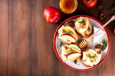 Sonbahar Elmalı Brie Crostini, Ceviz ve Bal, Sonbahar yemeği, Şükran Günü parti aperatifleri. Kırmızı elma dilimli küçük sandviçler, brie peyniri ve tatlı bal çiselemeleri.