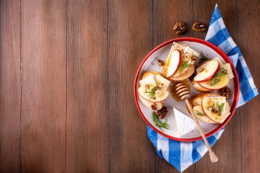 Sonbahar Elmalı Brie Crostini, Ceviz ve Bal, Sonbahar yemeği, Şükran Günü parti aperatifleri. Kırmızı elma dilimli küçük sandviçler, brie peyniri ve tatlı bal çiselemeleri.