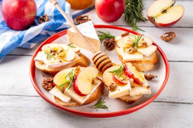 Sonbahar Elmalı Brie Crostini, Ceviz ve Bal, Sonbahar yemeği, Şükran Günü parti aperatifleri. Kırmızı elma dilimli küçük sandviçler, brie peyniri ve tatlı bal çiselemeleri.