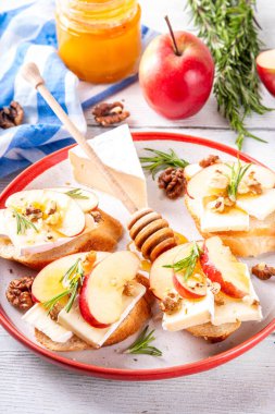 Sonbahar Elmalı Brie Crostini, Ceviz ve Bal, Sonbahar yemeği, Şükran Günü parti aperatifleri. Kırmızı elma dilimli küçük sandviçler, brie peyniri ve tatlı bal çiselemeleri.