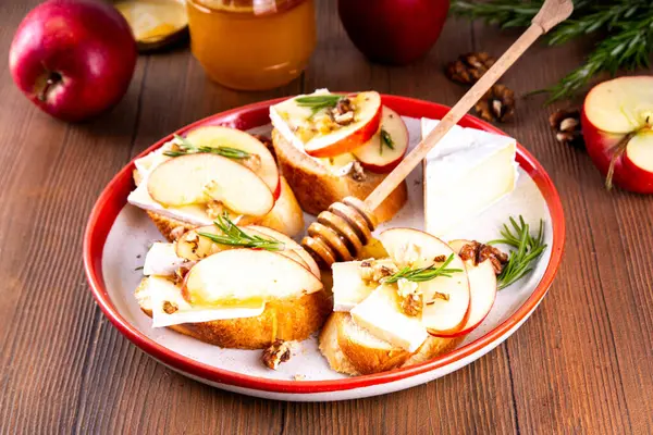 Sonbahar Elmalı Brie Crostini, Ceviz ve Bal, Sonbahar yemeği, Şükran Günü parti aperatifleri. Kırmızı elma dilimli küçük sandviçler, brie peyniri ve tatlı bal çiselemeleri.