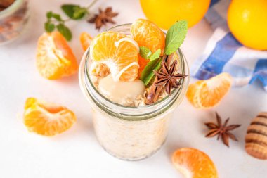 Mandalina kremalı bir gecelik yulaf ezmesi, kremalı yulaf ezmesi ve taze mandalina dilimleri, baharatlar ve portakal kabuğu.