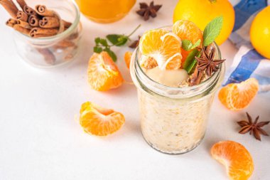 Mandalina kremalı bir gecelik yulaf ezmesi, kremalı yulaf ezmesi ve taze mandalina dilimleri, baharatlar ve portakal kabuğu.