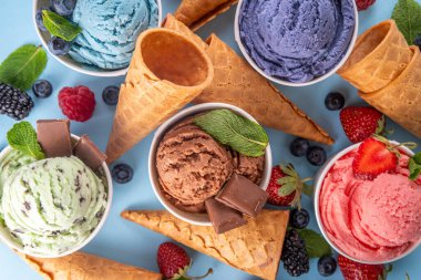 Renkli arka planda waffle konileri ve böğürtlenlerle dolu renkli, parlak dondurmalar. Taze böğürtlenli farklı aromalı dondurma porsiyonları üst görünüm kopya alanı arka planı