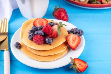 Yaz meyveli geleneksel Amerikan krepleri yığını. Sabah güneşinde bal, çilek ve yabanmersinli kahvaltı krepleri, mavi ahşap arka plan fotokopi alanı.
