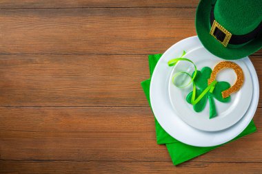 St. Patrick's Day festive table setting. Plate and cutlery with green napkin, shamrock symbol, gold horseshoe decor for luck. Patrick Day menu background, party invitation, top view copy space