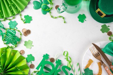 Saint Patrick masa takımı çatal bıçak, bıçak ve çatal, Patrick günü dekorasyonu, bozuk paralar, leprikon şapkası, gözlükler, şanslı at nalı, konfeti, yeşil arka planda boncuklar.