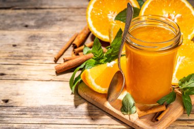 Homemade orange jam in small jar. Homemade orange spicy jam with fresh oranges, cinnamon, mint. Fall preparations and canning on wooden table background copy space