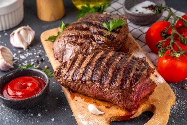 Ahşap kesme tahtasında ızgara biftek, ketçap sosu ve baharat, üst görünüm kopya alanı.