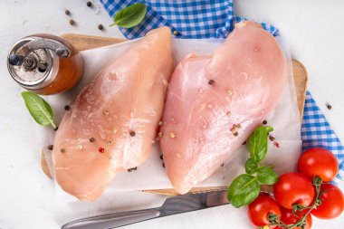 Mutfak masasında çiğ tavuk göğsü filetosu ve baharatlar. Beyaz yağsız et pişirme arka planı, beyaz masa kopyalama alanı