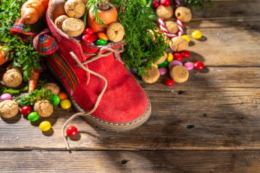 Sinterklaas, Saint Nicholas day background. Little kid red shoe with carrots and sweets, trooigoed, pepernoten, candy. Dutch Christmas holiday on cozy wooden background. 