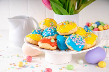 Paskalya bayramı dekoru ve bahar lale çiçeği buketiyle süslenmiş beyaz mutfak arka planında renkli şekerli ve serpiştirilmiş İtalyan Paskalya kurabiyeleri.