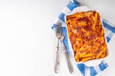 Fırınlanmış Ziti makarnası bolonez ya da marinara domates sosu ve peyniri, fırında tava ve tabakta, beyaz mutfak masasında fotokopi alanı.