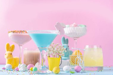 Colorful pastel colored kids Easter party mocktails, Creamy and iced non-alcohol drinks with cotton candy, marshmallow, sugar sprinkles and Easter eggs, on blue pink pastel background copy space