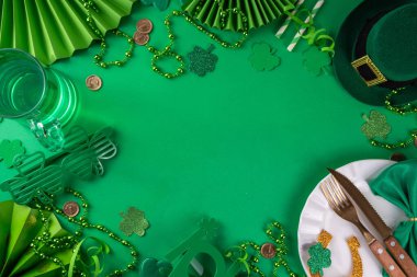 Saint Patrick masa takımı çatal bıçak, bıçak ve çatal, Patrick günü dekorasyonu, bozuk paralar, leprikon şapkası, gözlükler, şanslı at nalı, konfeti, yeşil arka planda boncuklar.