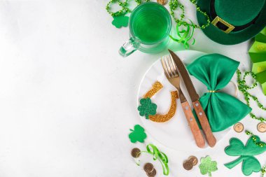 Saint Patrick masa takımı çatal bıçak, bıçak ve çatal, Patrick günü dekorasyonu, bozuk paralar, leprikon şapkası, gözlükler, şanslı at nalı, konfeti, yeşil arka planda boncuklar.