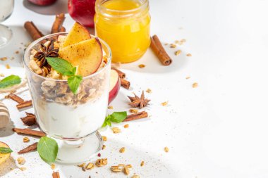 Apple Pie Granola Cheesecake, breakfast snack layered dessert with oat granola, cream cheese yogurt, honey, apple slices and cinnamon spices on white background copy space