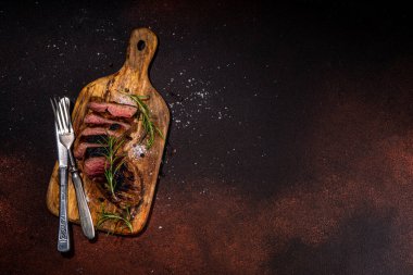 Grilled meat steak on dark table, Pork, veal, lamb, beef steak medium, medium well on cutting board, with spices, ketchup bbq sauce, wine glass. Dinner in steak restaurant menu, top view copy space