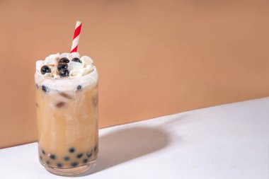 Klasik boba köpüklü çay tapyoka incileri ve sütsüz krema bardağın üstünde, yaz soğuk tatlı içeceği beyaz masa arkasında fotokopi alanı