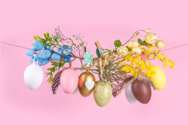 Yaratıcı, parlak bahar Paskalya tatili konsepti. Boyalı Paskalya yumurtaları, bahar çiçekleri, yapraklar ve dekorasyonlar çamaşır ipine asılı, parlak güneşli ışık fotokopi alanı rengarenk arka planda