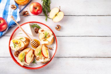 Sonbahar Elmalı Brie Crostini, Ceviz ve Bal, Sonbahar yemeği, Şükran Günü parti aperatifleri. Kırmızı elma dilimli küçük sandviçler, brie peyniri ve tatlı bal çiselemeleri.