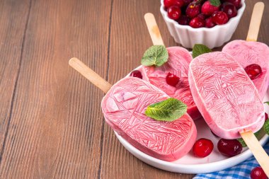 Yabanmersinli dondurma, dondurulmuş kremalı dondurma yoğurt ve böğürtlenli lolipoplar, beyaz tabakta, taze yaban mersinli ve nane yapraklı. 