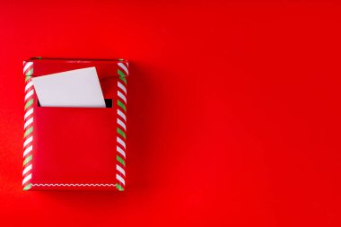 Noel kutlaması için hazırlık. Noel Baba geleneğine mektup yazıyorum. Kırmızı arka planda küçük kırmızı çizgili posta kutusu, zarflar ve Noel süslemeleri. 