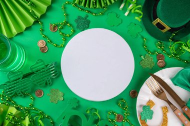 Saint Patrick masa takımı çatal bıçak, bıçak ve çatal, Patrick günü dekorasyonu, bozuk paralar, leprikon şapkası, gözlükler, şanslı at nalı, konfeti, yeşil arka planda boncuklar.