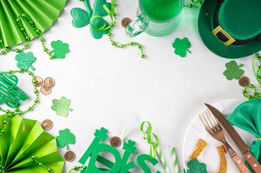 Saint Patrick masa takımı çatal bıçak, bıçak ve çatal, Patrick günü dekorasyonu, bozuk paralar, leprikon şapkası, gözlükler, şanslı at nalı, konfeti, yeşil arka planda boncuklar.