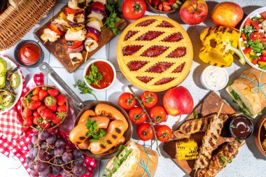 Çeşitli piknik barbekü yemekleri ve flatlay içiyorlar. Yaz bbq piknik yemekleri, ızgara etler, kebaplar, sebzeler, meyve salatası, geleneksel piknik pastası, sandviçler, üst görünüm fotokopi alanı.