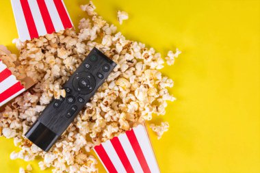 Renkli parlak arka planda televizyon kumandalı kağıt kaseler dolusu patlamış mısır. Televizyon, film galası, TV dizisi, spor, dizi izlemenin tadını çıkarın. Düz yatış, üst görünüm 