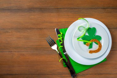 St. Patrick's Day festive table setting. Plate and cutlery with green napkin, shamrock symbol, gold horseshoe decor for luck. Patrick Day menu background, party invitation, top view copy space
