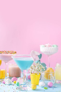 Colorful pastel colored kids Easter party mocktails, Creamy and iced non-alcohol drinks with cotton candy, marshmallow, sugar sprinkles and Easter eggs, on blue pink pastel background copy space