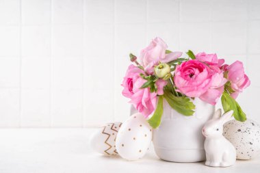 Bahar Paskalya bayramı masası boyalı Paskalya yumurtaları, pembe bahar çiçekleri, seramik dekorlu tavşanlar beyaz mutfak arka planında fotokopi alanı