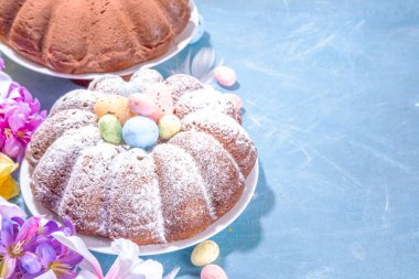 Traditional cake for Easter. Chocolate and vanilla Easter round cake with chocolate and sugar powder sprinkles, colorful Easter eggs, spring flowers, on a blue background copy space