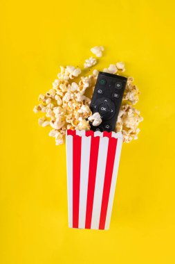 Renkli parlak arka planda televizyon kumandalı kağıt kaseler dolusu patlamış mısır. Televizyon, film galası, TV dizisi, spor, dizi izlemenin tadını çıkarın. Düz yatış, üst görünüm 