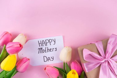 Anneler gününde lale çiçeği buketi, pembe kurdeleli hediye kutusu ve mutlu anneler günü etiketi. Tebrik kartı arkaplanı, poster, broşür, broşür, tanıtım malzemeleri, web sitesi