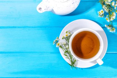 Bitkisel organik papatya çayı ve taze vahşi yaz papatya çiçekleri, beyaz fincanda, çaydanlık kopyasıyla birlikte.