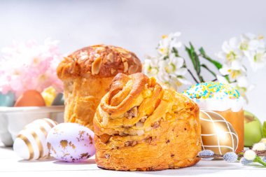 Easter baking background with traditional holiday cakes - kraffin, panettone, paska kulich, with Easter eggs, spring flowers on white wooden table, spring holiday Easter greeting card background clipart