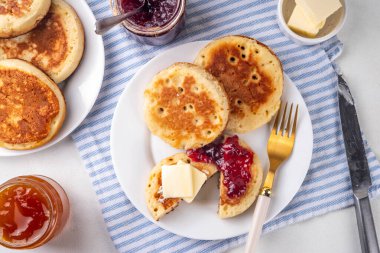 Traditional English skillet fried breakfast pastry Crumpets, popular in England, Britain pancakes. Sweet hot crumpets stack with melting butter and jam clipart