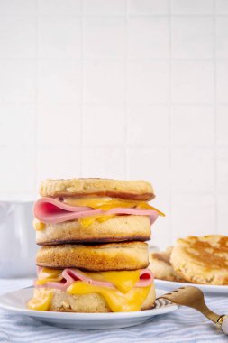 Breakfast crumpet sandwich, british pancake scones burger with cheese and ham, on itchen table, with stack of crumpets and butter clipart