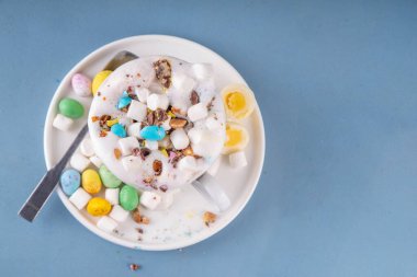 Krem şantili Paskalya sıcak çikolatası, marşmelov ve ezilmiş çikolatalı mini yumurtalar, renkli masa arkaplanında, malzemelerle, kopyalama alanı