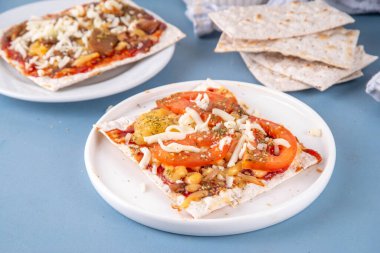 Açık mavi arkaplanda, içinde malzemeler, peynir ve domates sosu olan Matzah Pizza. Yahudi Pesach ve Hamursuz Bayramı için gıda fikirleri ve tarifi