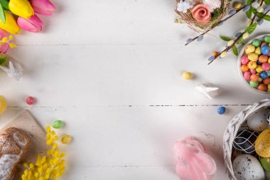 Tatlı Paskalya bayramı tebrik kartı geçmişi. Tavşan desenli renkli Paskalya yumurtaları, beyaz ahşap masa zemininde bahar çiçekleri, kopyalama alanı