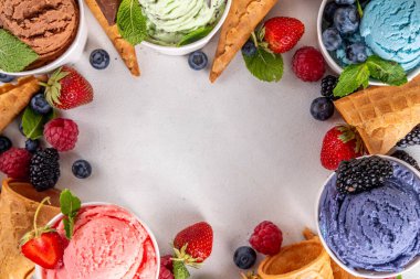Beyaz arka planda waffle külahları ve böğürtlenlerle dolu renkli dondurmalar. Taze böğürtlenli farklı aromalı dondurma porsiyonları üst görünüm kopya alanı arka planı