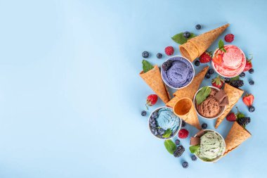 Renkli arka planda waffle konileri ve böğürtlenlerle dolu renkli, parlak dondurmalar. Taze böğürtlenli farklı aromalı dondurma porsiyonları üst görünüm kopya alanı arka planı