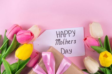 Anneler gününde lale çiçeği buketi, pembe kurdeleli hediye kutusu ve mutlu anneler günü etiketi. Tebrik kartı arkaplanı, poster, broşür, broşür, tanıtım malzemeleri, web sitesi