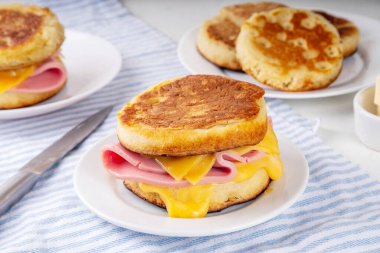 Breakfast crumpet sandwich, british pancake scones burger with cheese and ham, on itchen table, with stack of crumpets and butter clipart