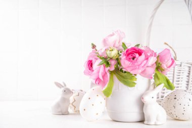 Bahar Paskalya bayramı masası boyalı Paskalya yumurtaları, pembe bahar çiçekleri, seramik dekorlu tavşanlar beyaz mutfak arka planında fotokopi alanı