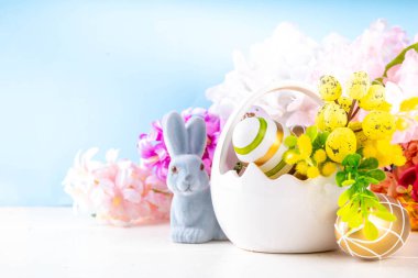 Tatlı Paskalya bayramı tebrik kartı geçmişi. Renkli Paskalya yumurtaları sepetin içinde tavşan dekoru, bahar çiçekleri beyaz tahta masa arka planında, kopyalama alanı